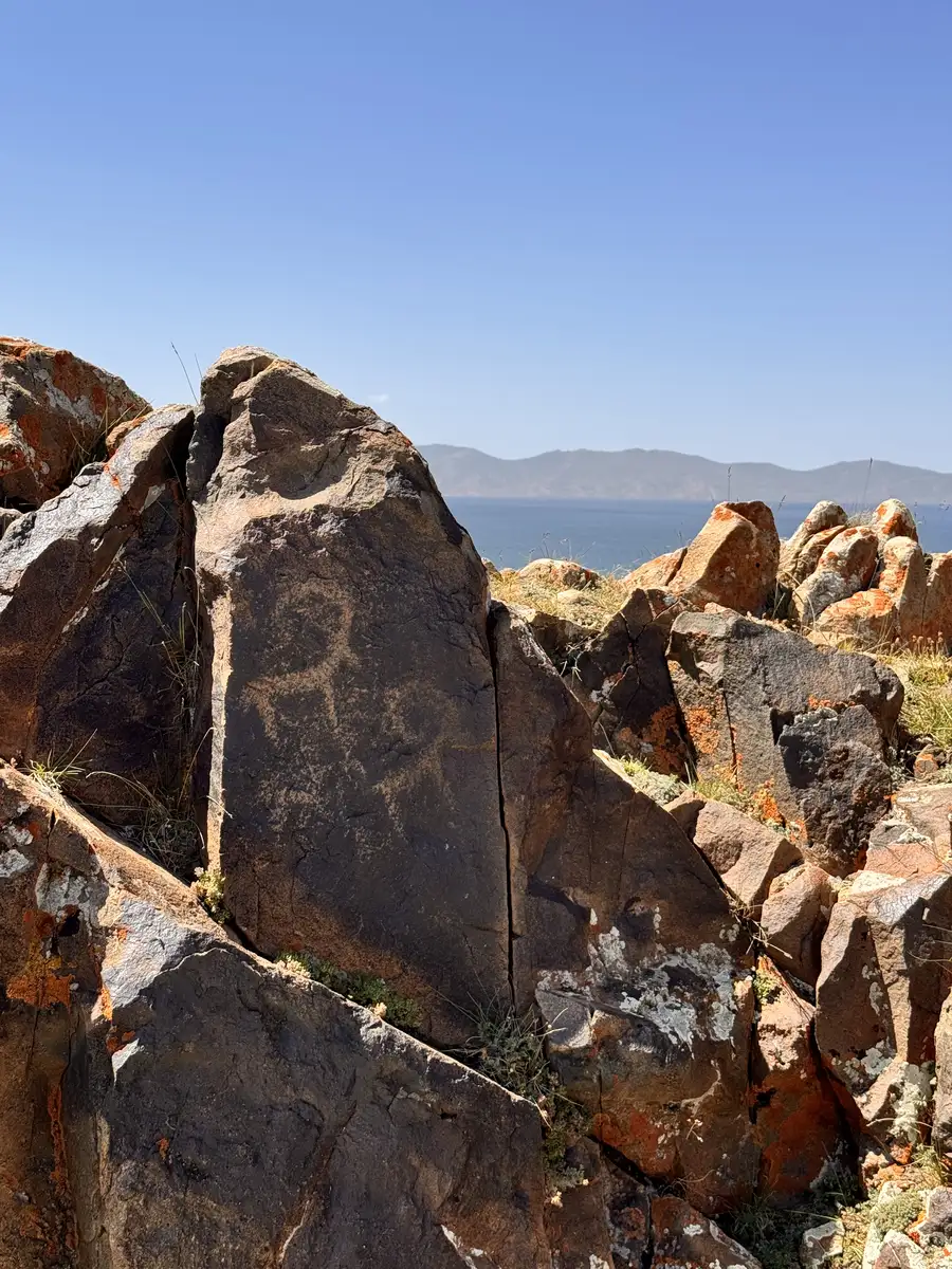 Ancient petroglyph carvings on boulders overlooking a lake and mountains